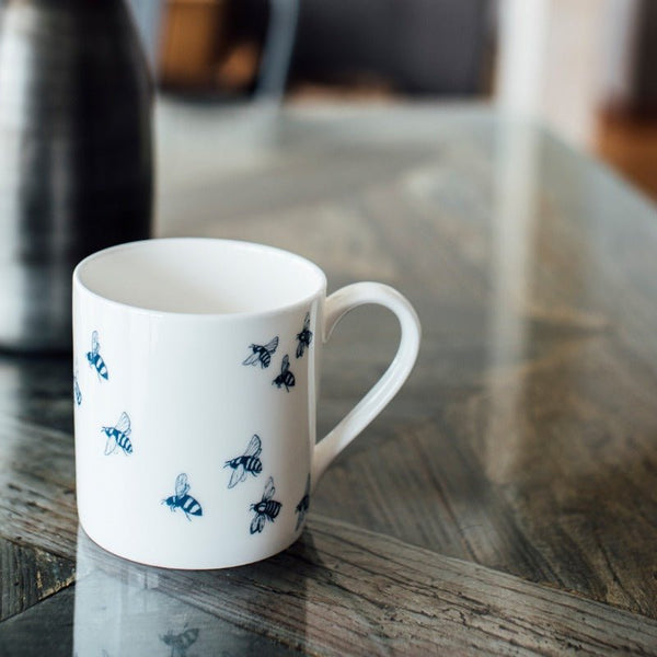 White fine bone china bee mug with blue bees from the Honey Bee Collection by Helen Round. Dishwasher safe.